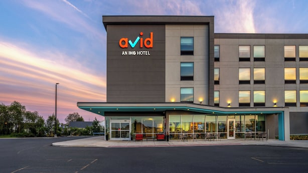 Un bâtiment moderne avec une enseigne indiquant « avid, un hôtel du groupe IHG », et un espace extérieur abrité avec des sièges.