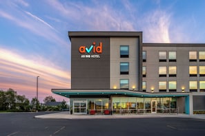 Un edificio moderno con la señalización 'avid AN IHG HOTEL' y una zona de estar cubierta al aire libre.