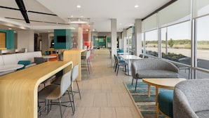 Un hall d’hôtel moderne doté d’un long comptoir d’accueil, d’un espace salon et de grandes fenêtres offrant une vue sur l’extérieur.