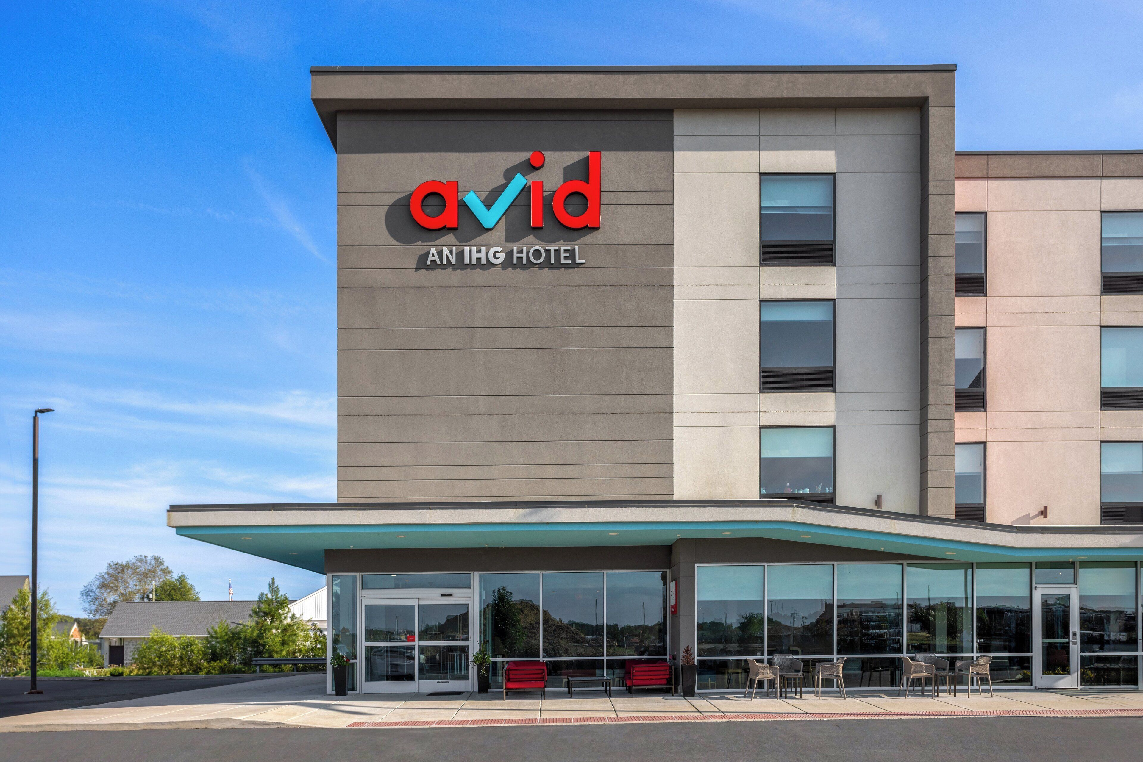 The exterior of the Avid An IHG Hotel with a modern design, large windows, and a covered entrance area.