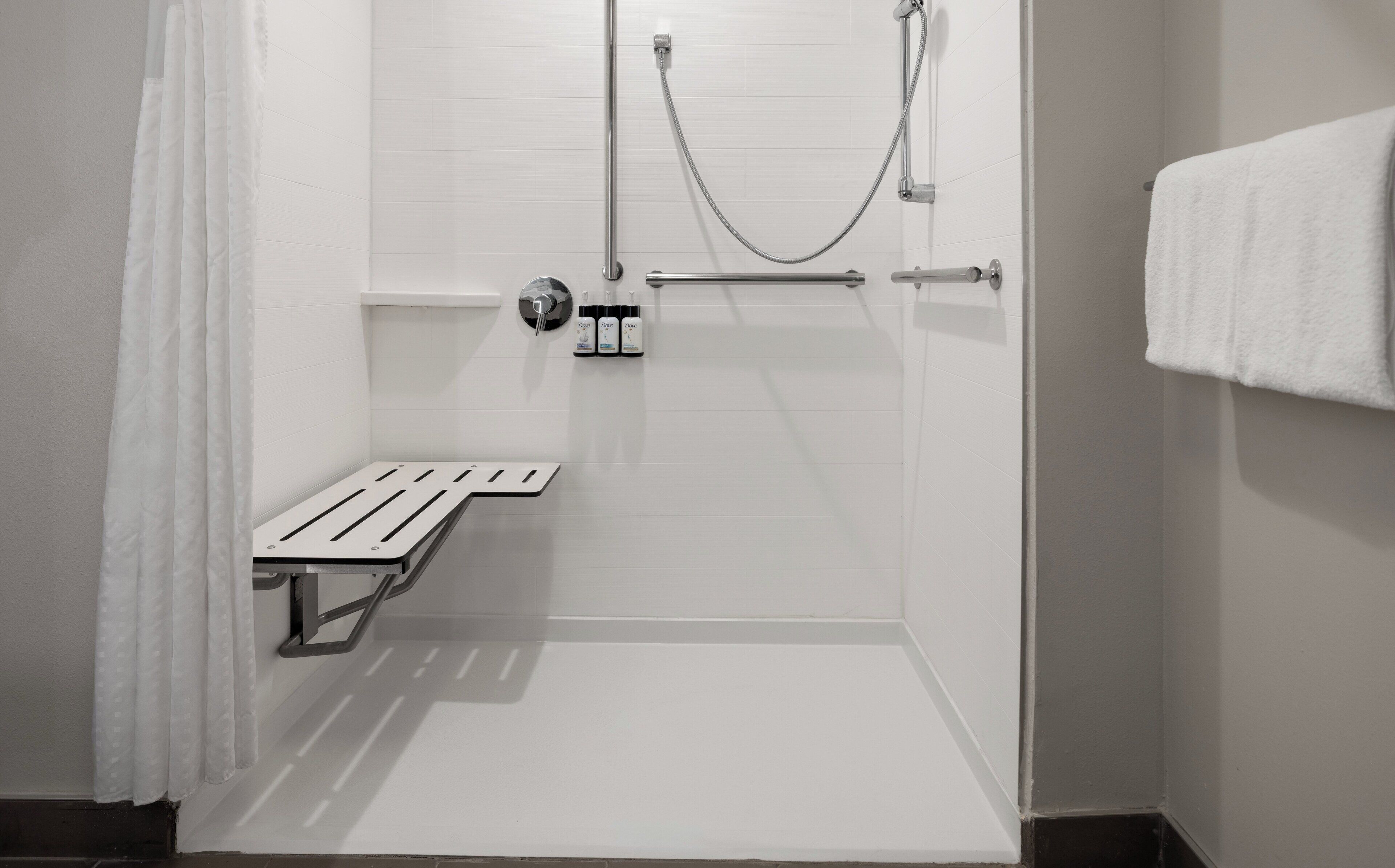 Una cabina doccia piccola e bianca, con una panchina, un porta asciugamani e un soffione erogatore manuale.