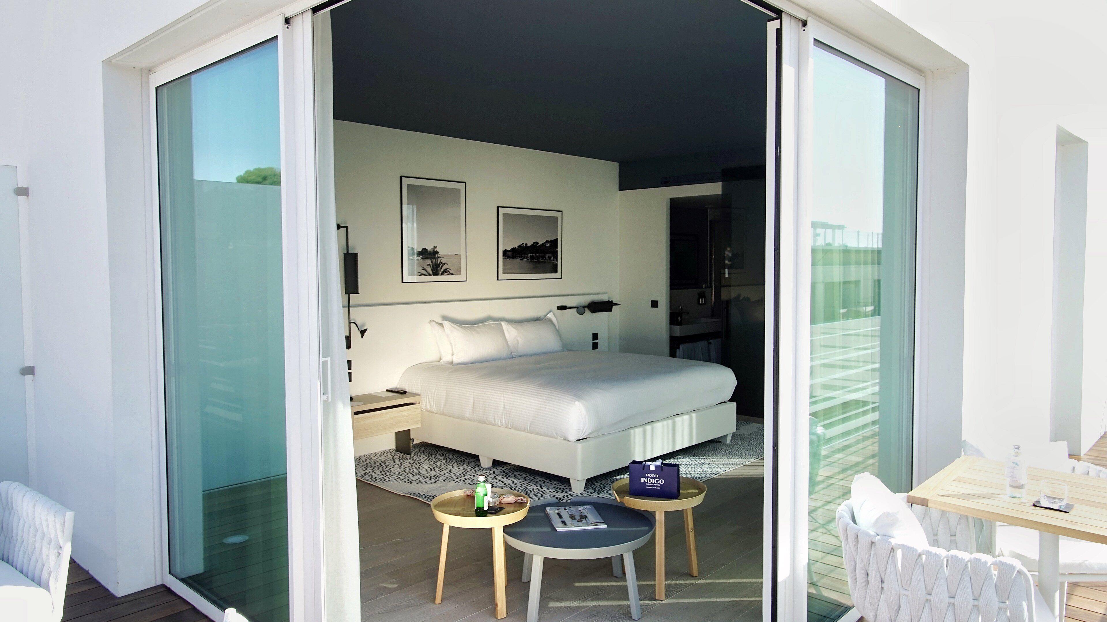 Une chambre à coucher moderne avec un grand lit, une table de chevet, une petite table sur laquelle se trouvent une bouteille et un livre, et une chaise.