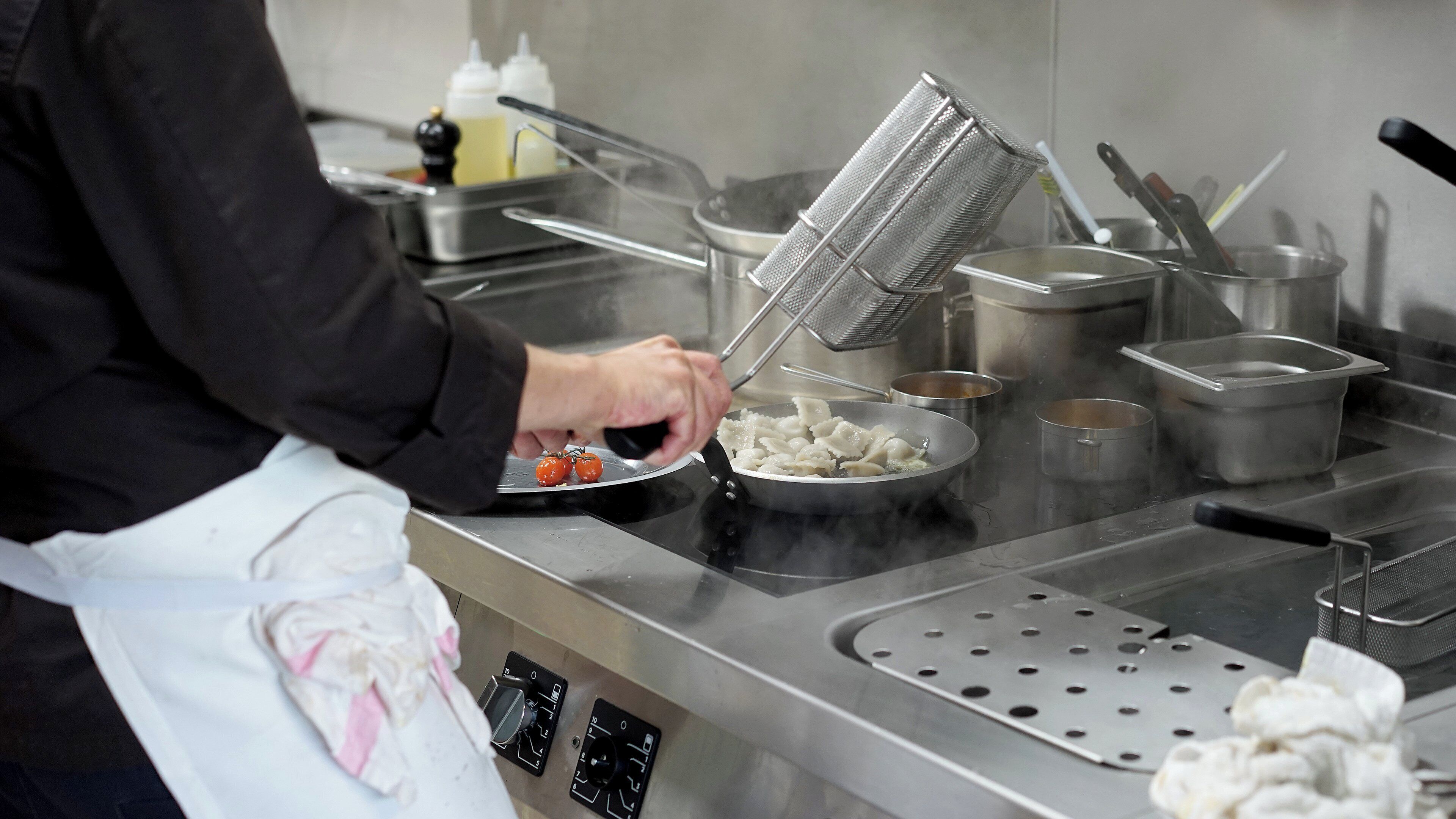 A kitchen with stainless steel appliances, a person cooking, and various cooking utensils.