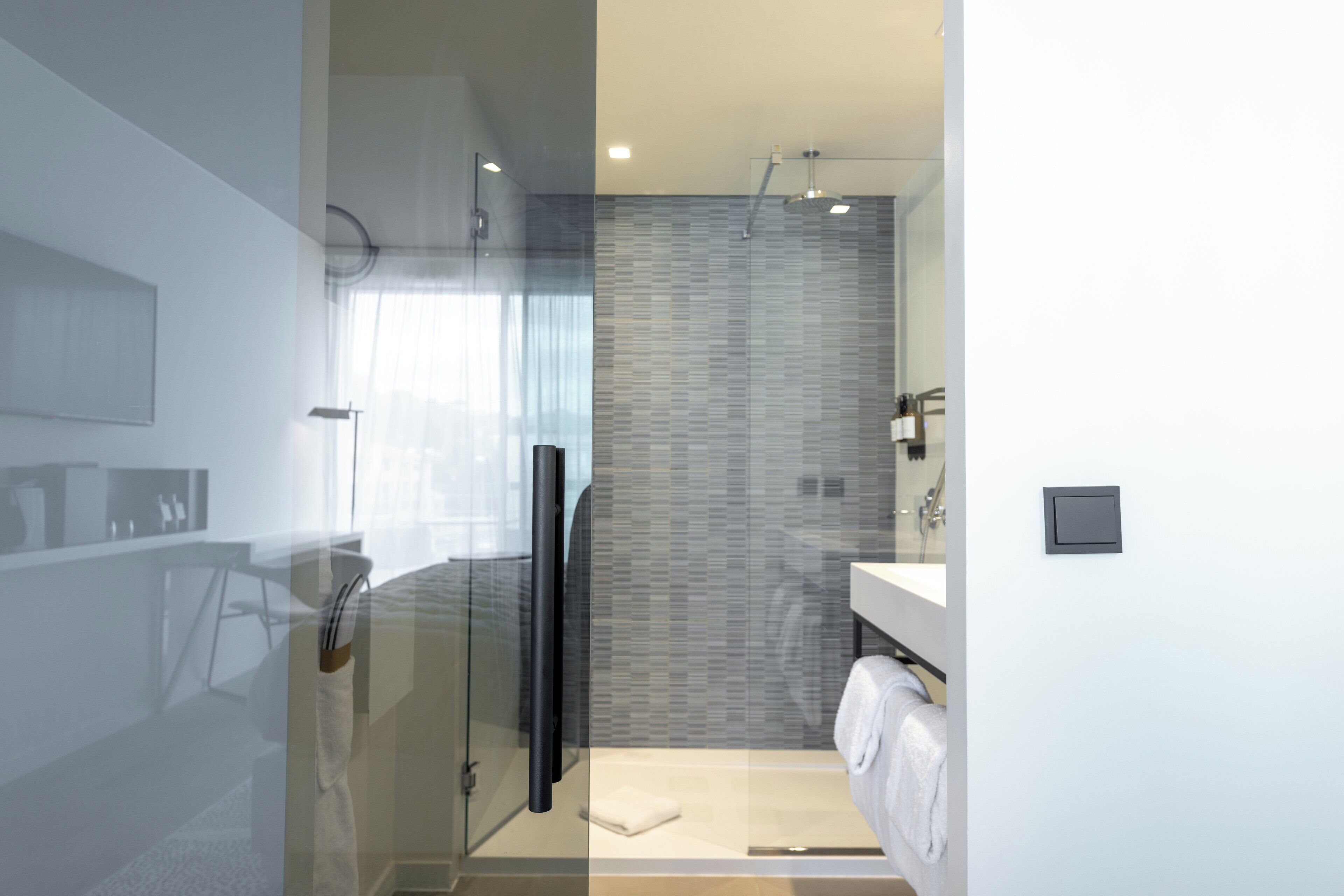 A modern bathroom with a glass shower enclosure, a white sink, and a tiled shower wall.