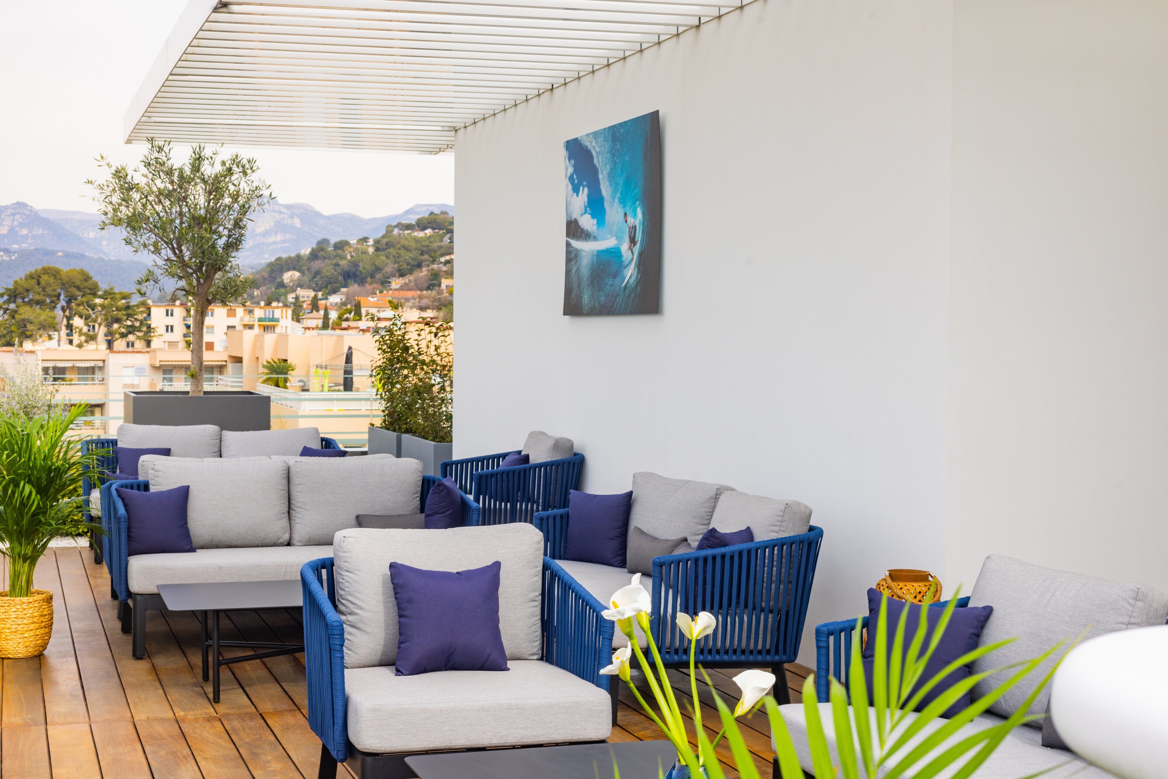 A terrace with outdoor seating, a potted plant, and a view of the city and mountains.