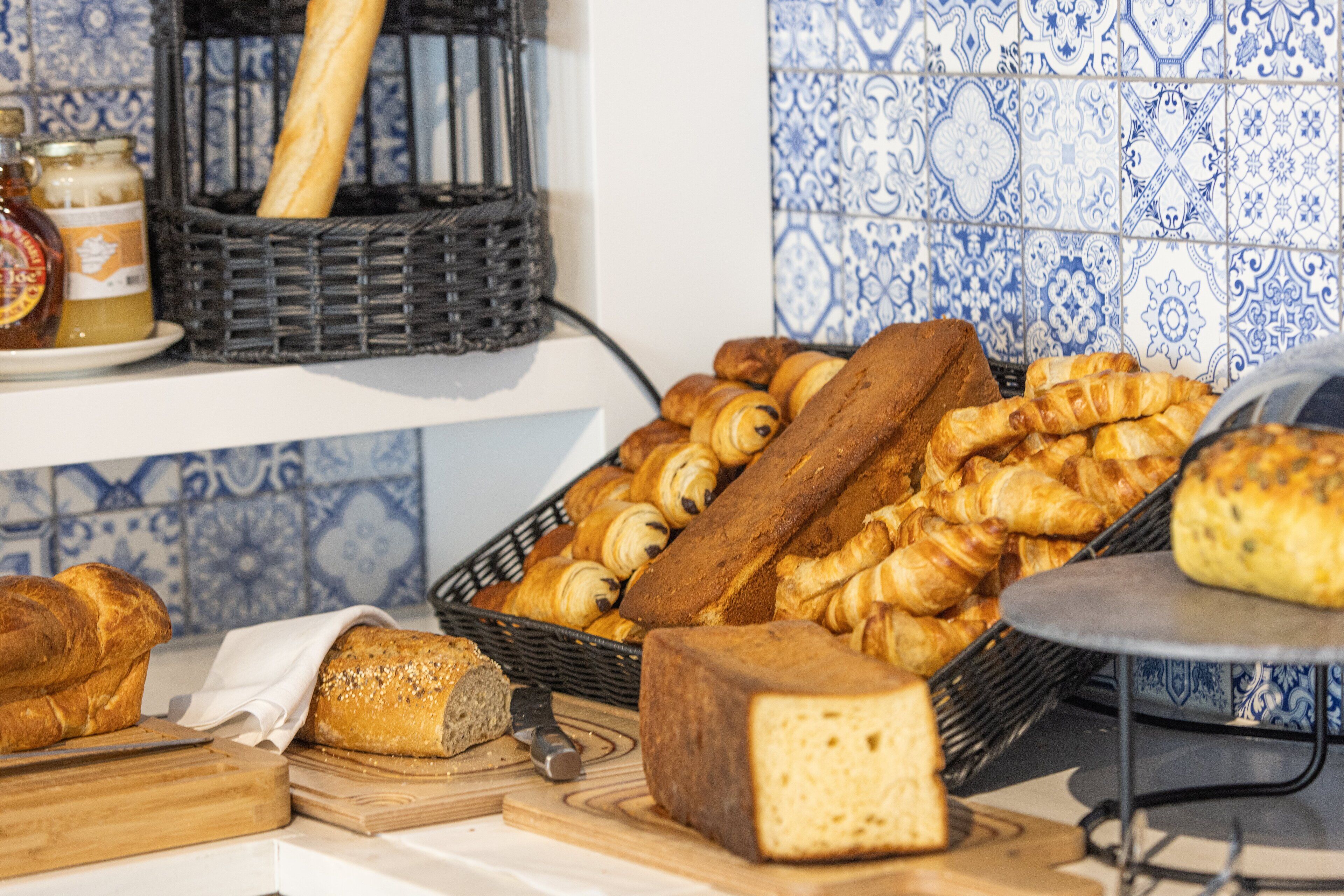 Une variété de pains et de viennoiseries sont disposés sur un plan de travail de cuisine, notamment des croissants et une miche de pain.