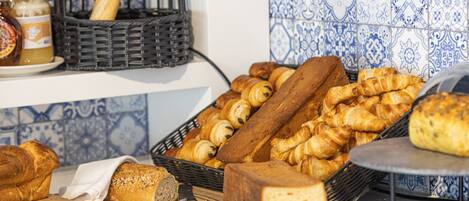 Une variété de pains et de viennoiseries sont disposés sur un plan de travail de cuisine, notamment des croissants et une miche de pain.