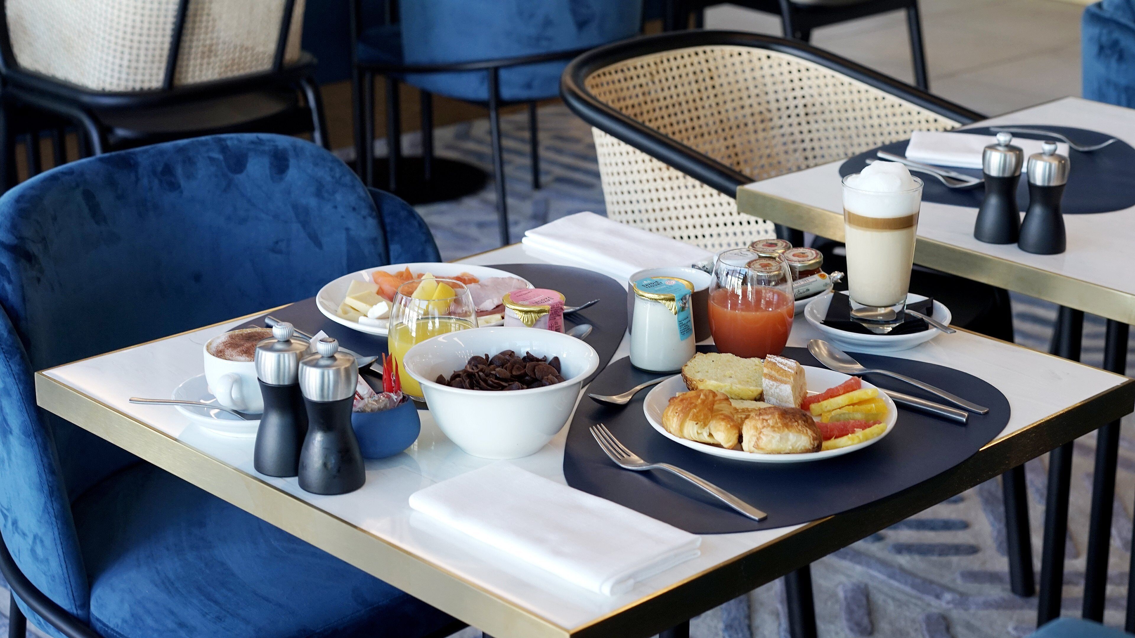 A breakfast setting with a variety of food items and beverages on a table, including a bowl of chocolate, a plate of croissants, and a glass of orange juice.
