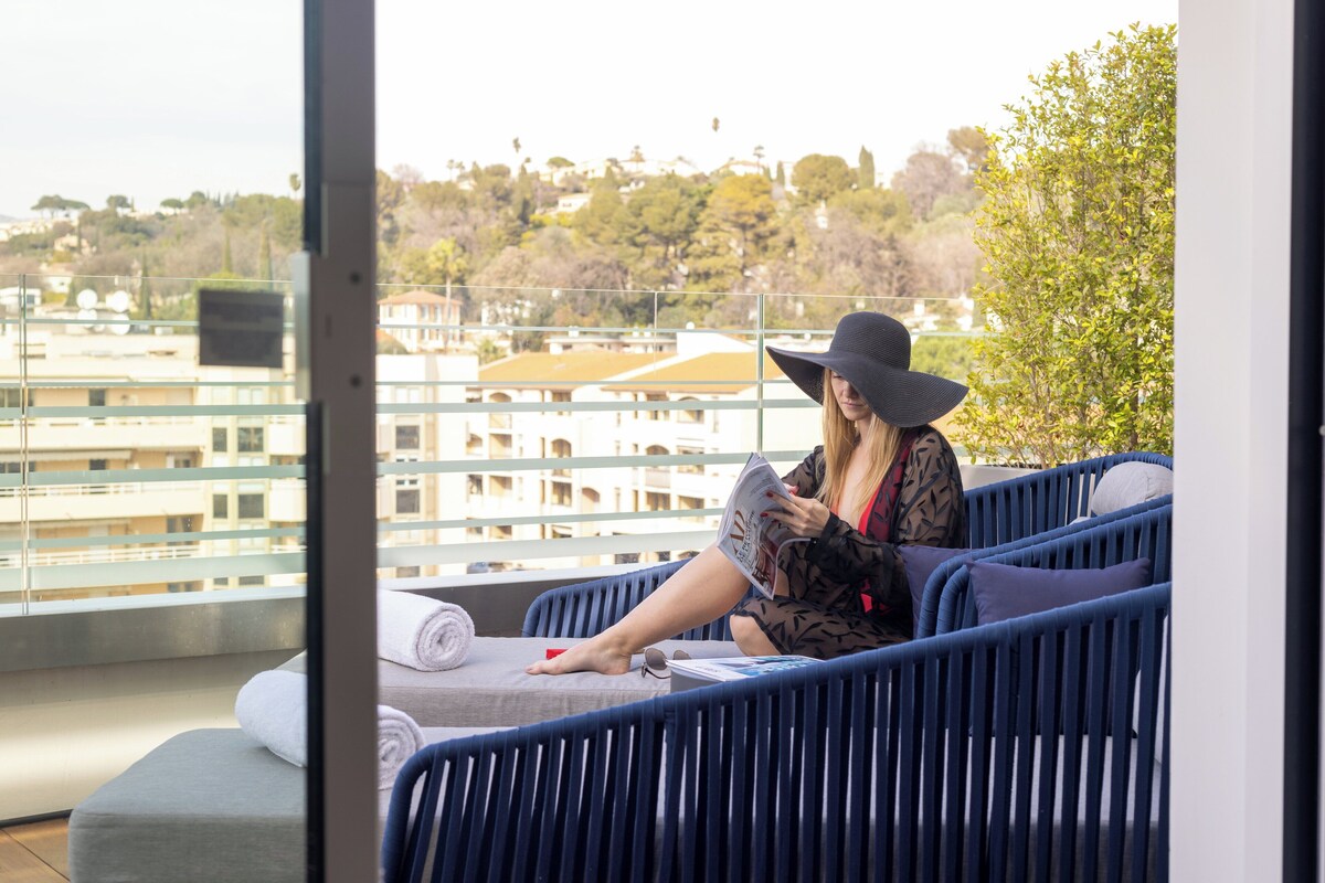 A person sitting on a blue chair with a view of buildings and trees in the background.