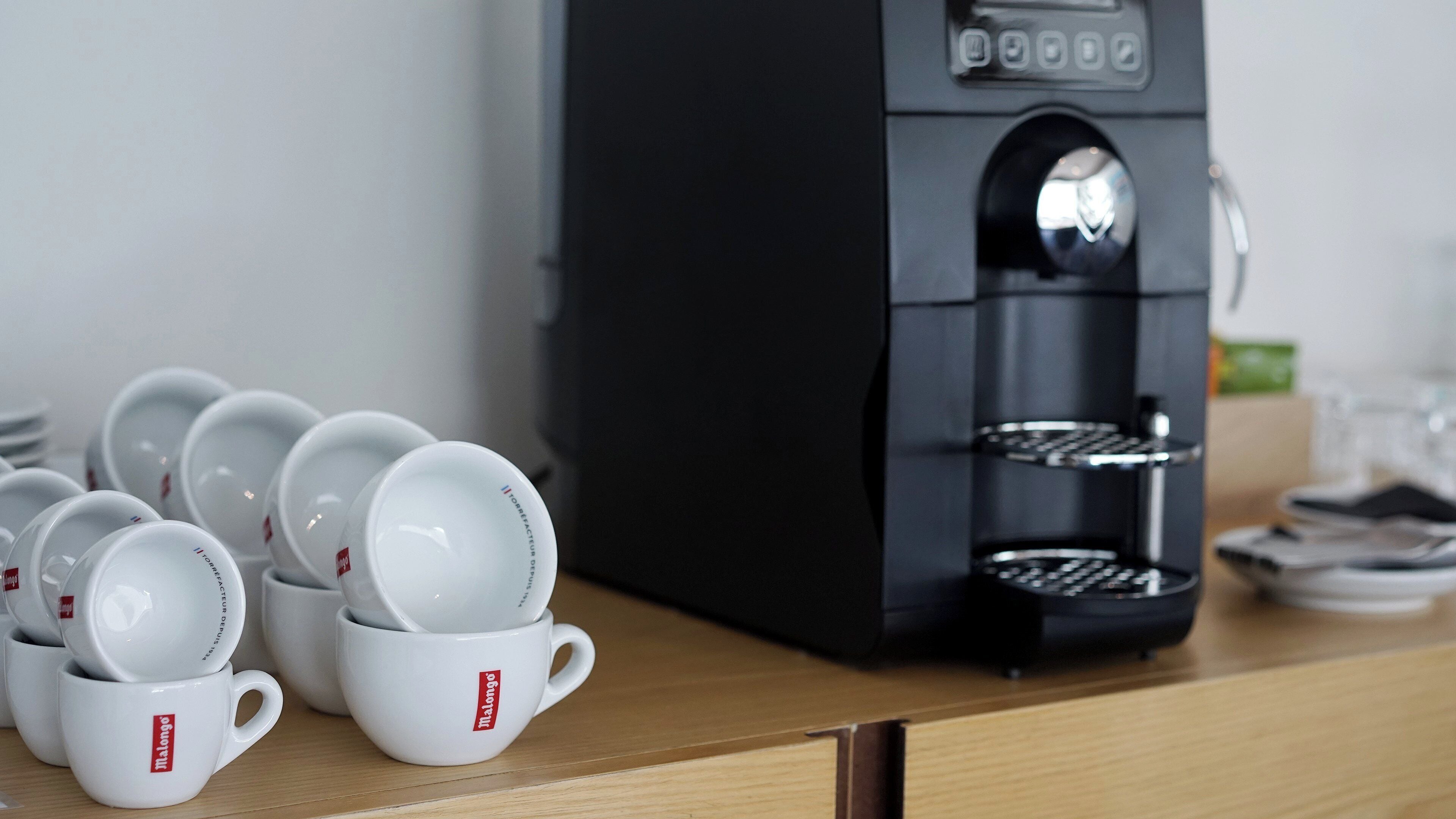 Una cafetera con varias tazas apiladas al frente.