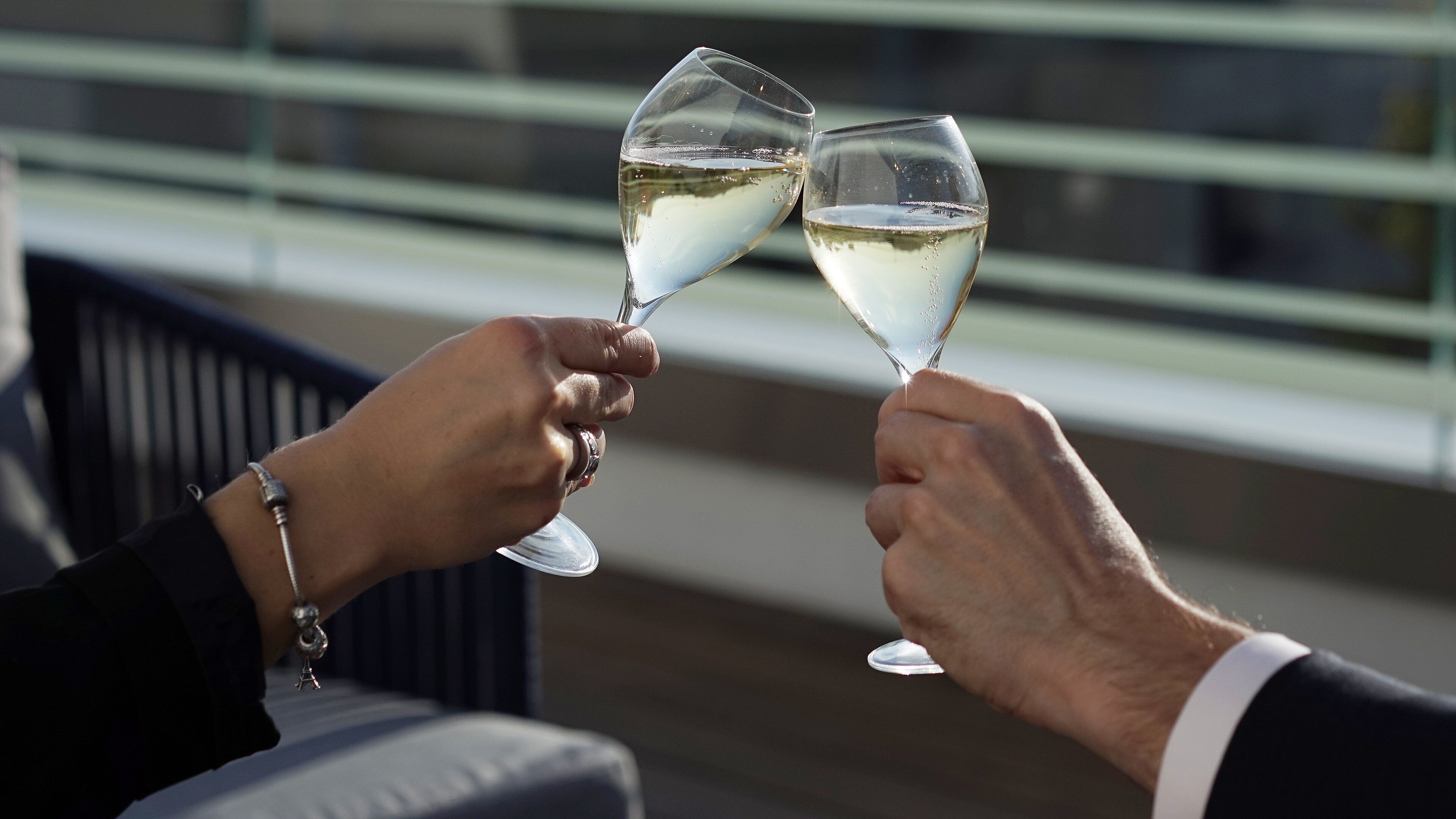 Two people toasting with champagne glasses on a balcony with a railing.