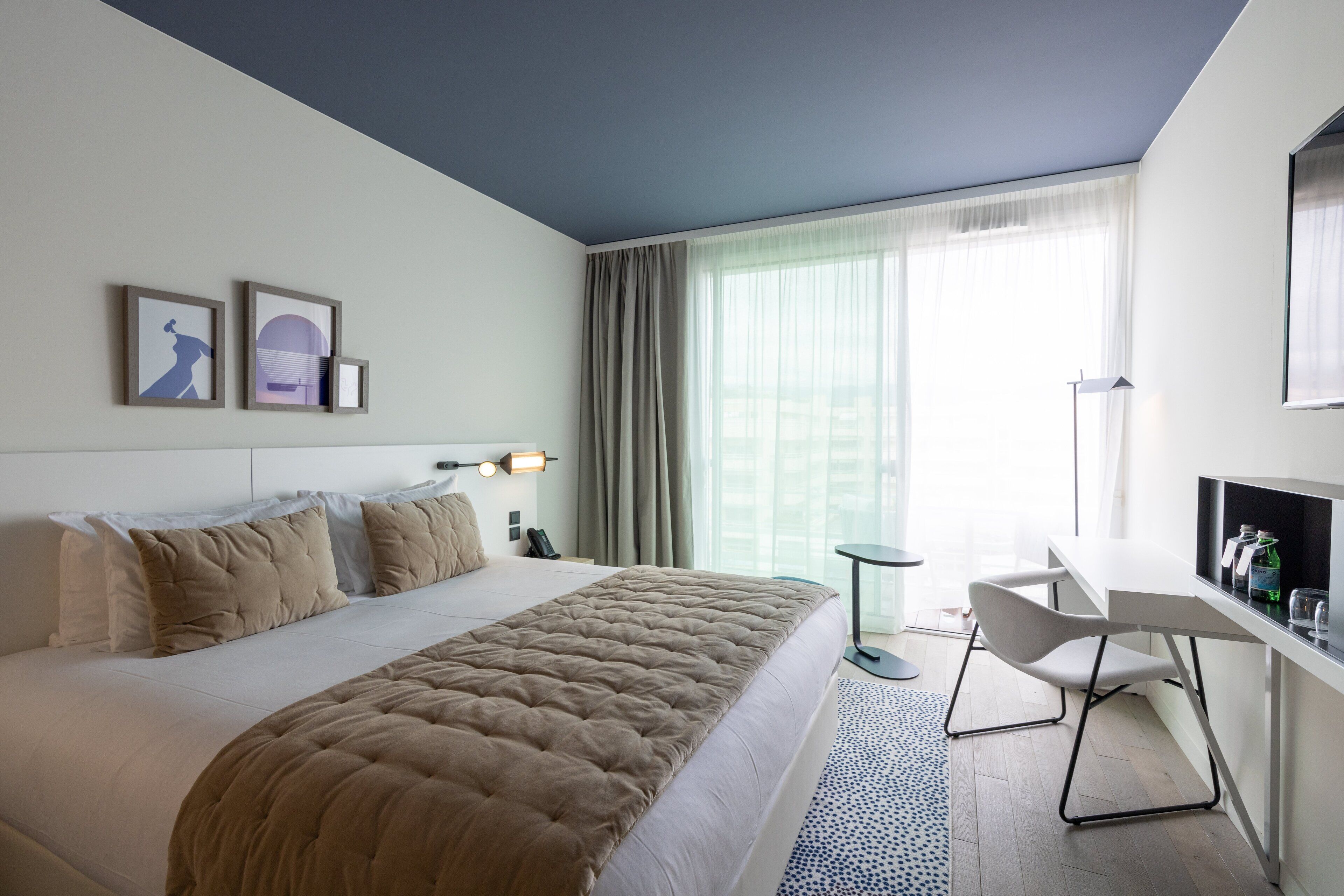 A modern hotel room with a large bed, a desk, and a view of the city.
