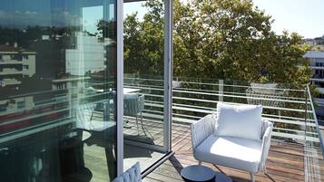 Ein moderner Balkon mit einem weißen Sitzmöbel, einem kleinen runden Tisch und einem Glasgeländer.