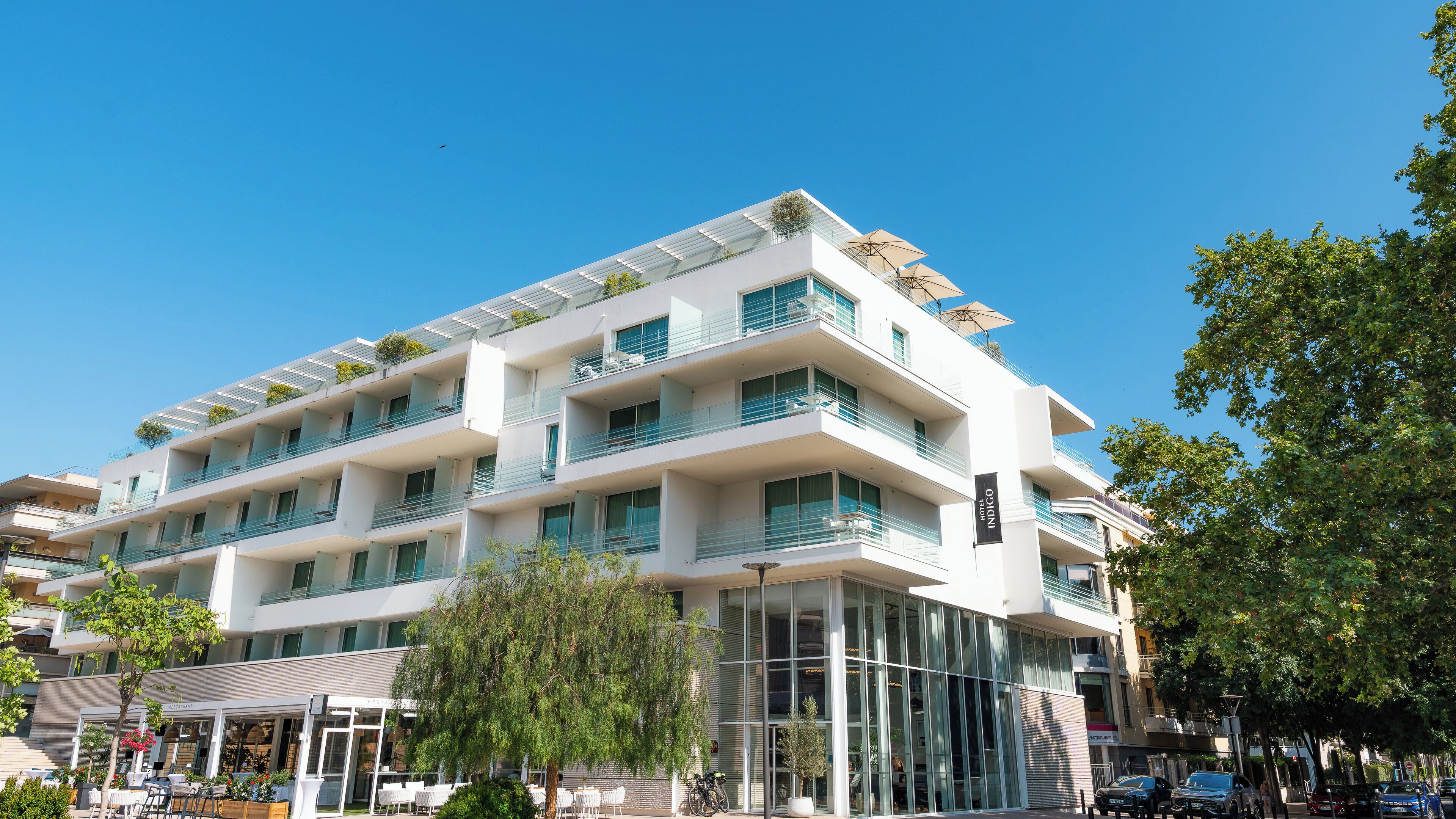 Un hôtel à plusieurs étages doté de balcons, d’une façade en verre et d’un espace extérieur aménagé pour s’asseoir.