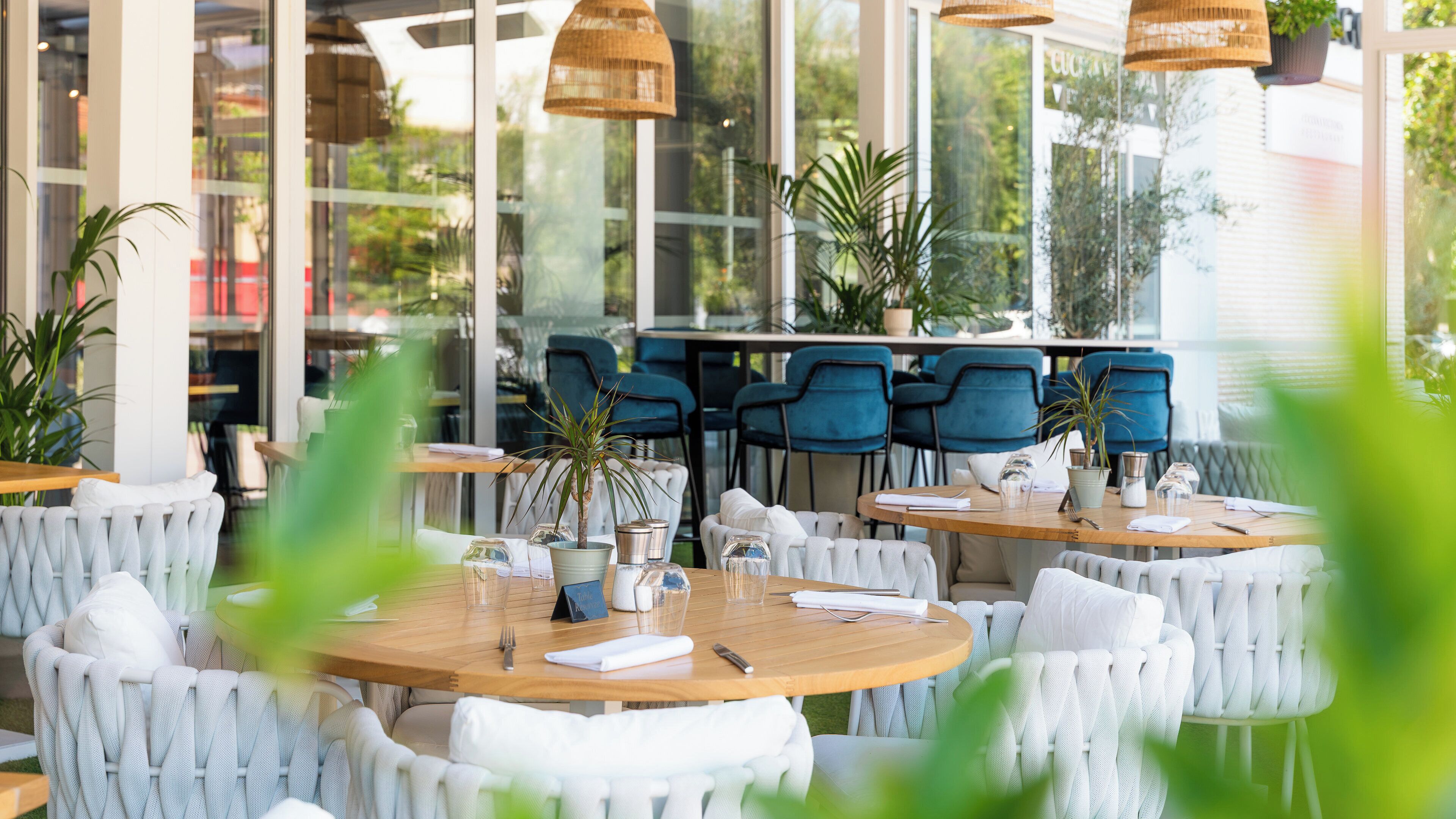 Ein Restaurant mit runden Tischen, weiß gepolsterten Stühlen und hängenden Korbtischen.