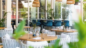 A restaurant with round tables, white cushioned chairs, and hanging wicker lamps. - Hotel Indigo Cagnes-sur-Mer by IHG (Cagnes-sur-Mer)