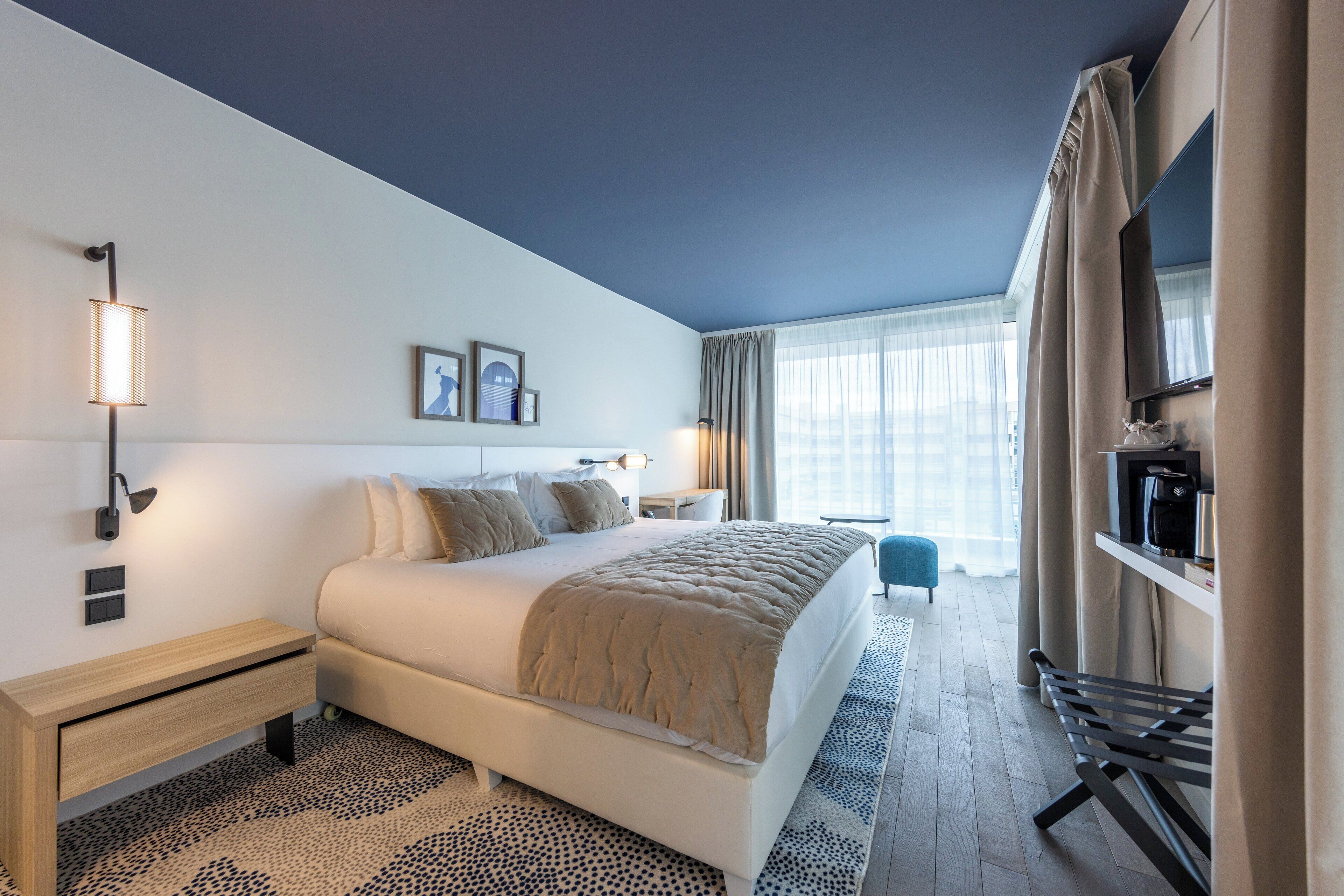 Una habitación de hotel moderna con una cama grande, mesitas de noche, un televisor y vistas a la ciudad.