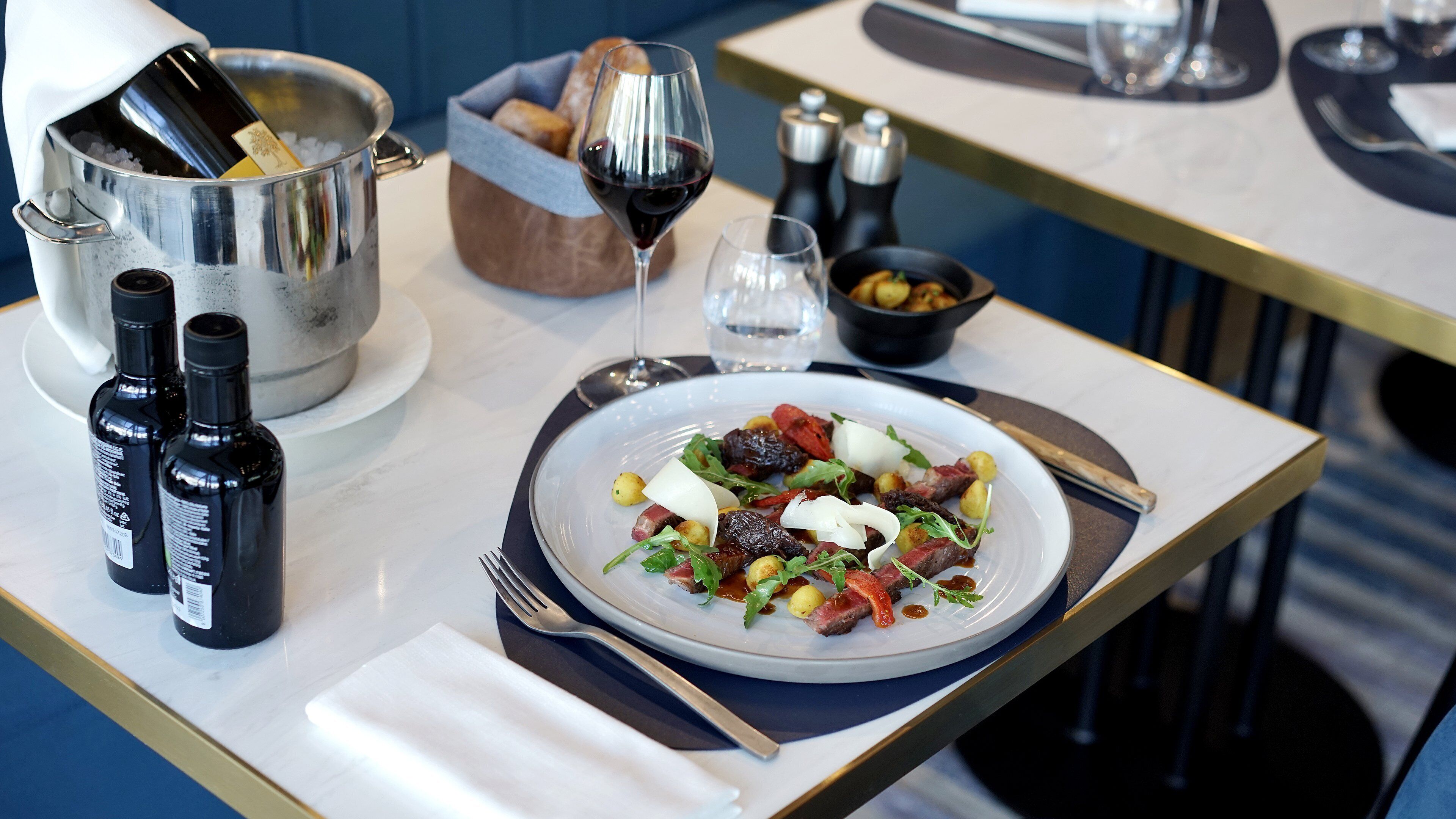 A dining table with a plate of food, wine bottles, a salt and pepper set, and a bread basket.
