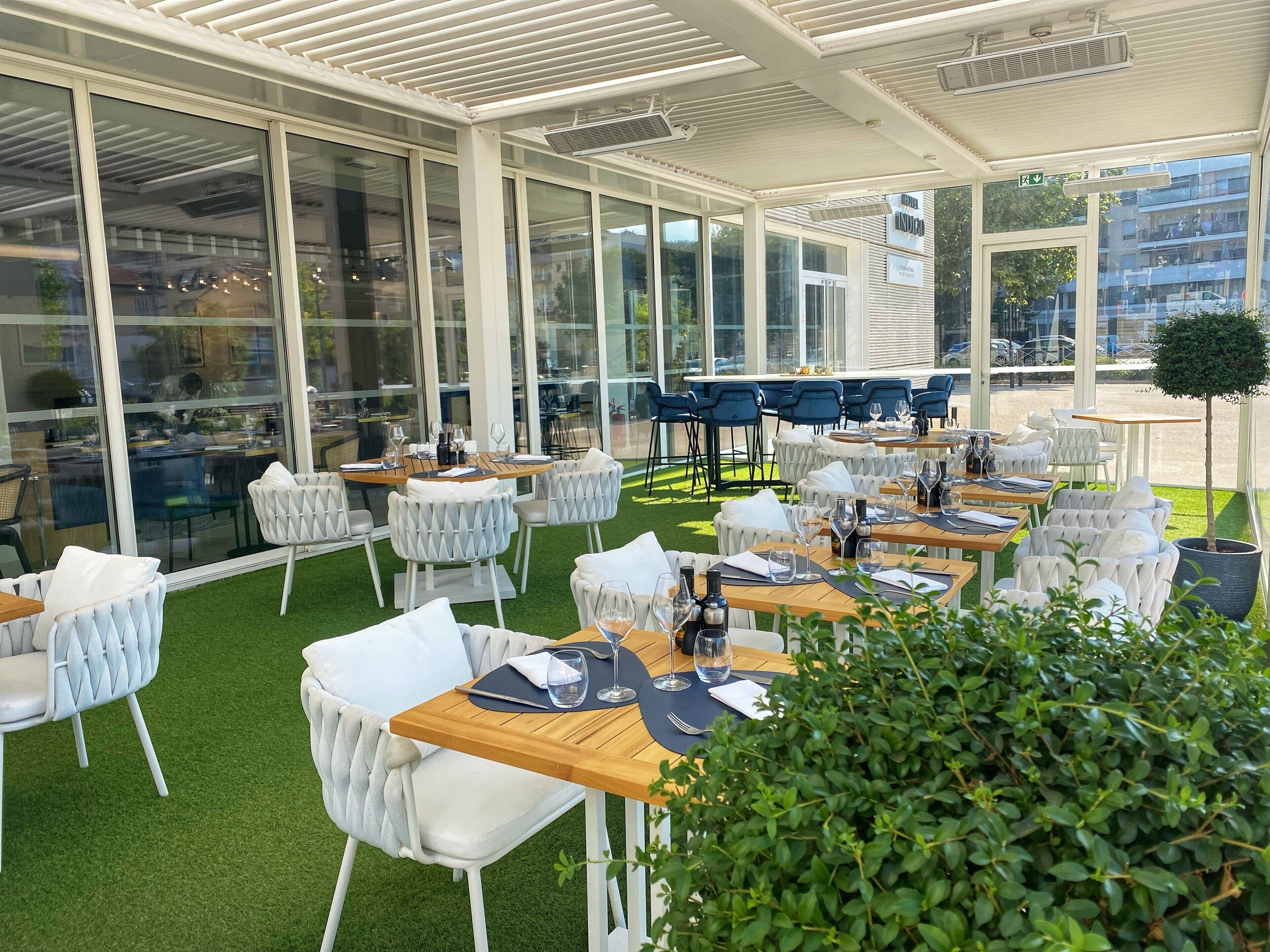 An outdoor dining area with tables and chairs, large windows, and a view of the street.