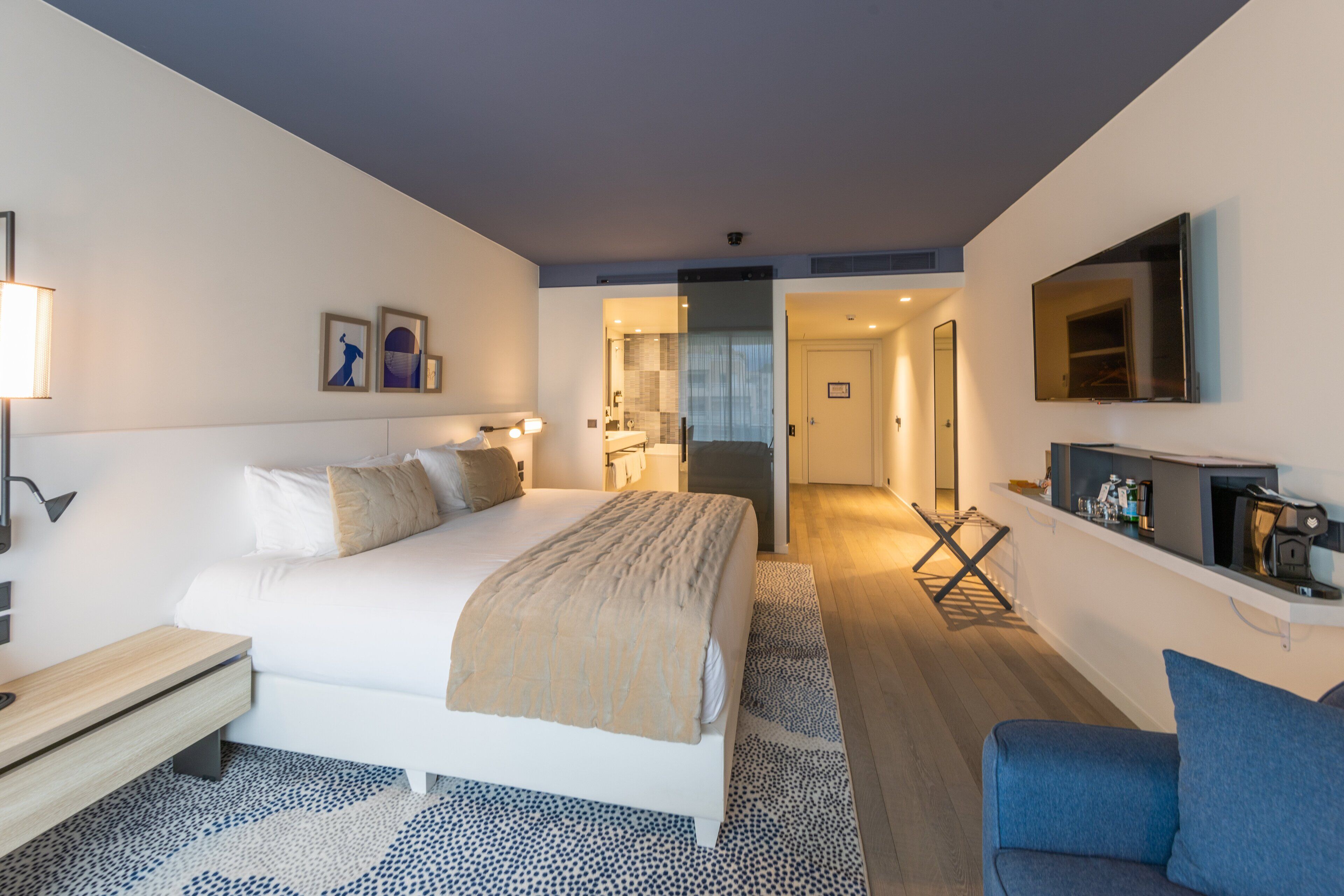 Une chambre d’hôtel moderne avec un grand lit, une table de chevet et un téléviseur fixé au mur.