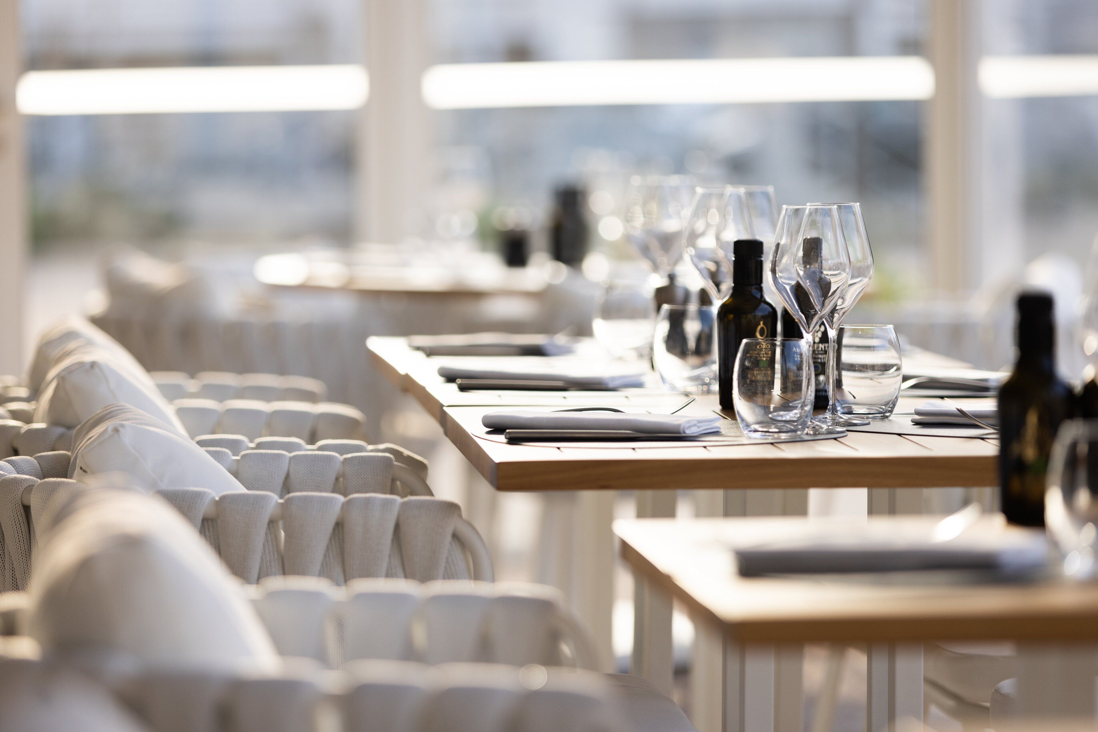Un ambiente de restaurante con mesas dispuestas para comer, con sillas blancas y una presentación de mesa impecable.