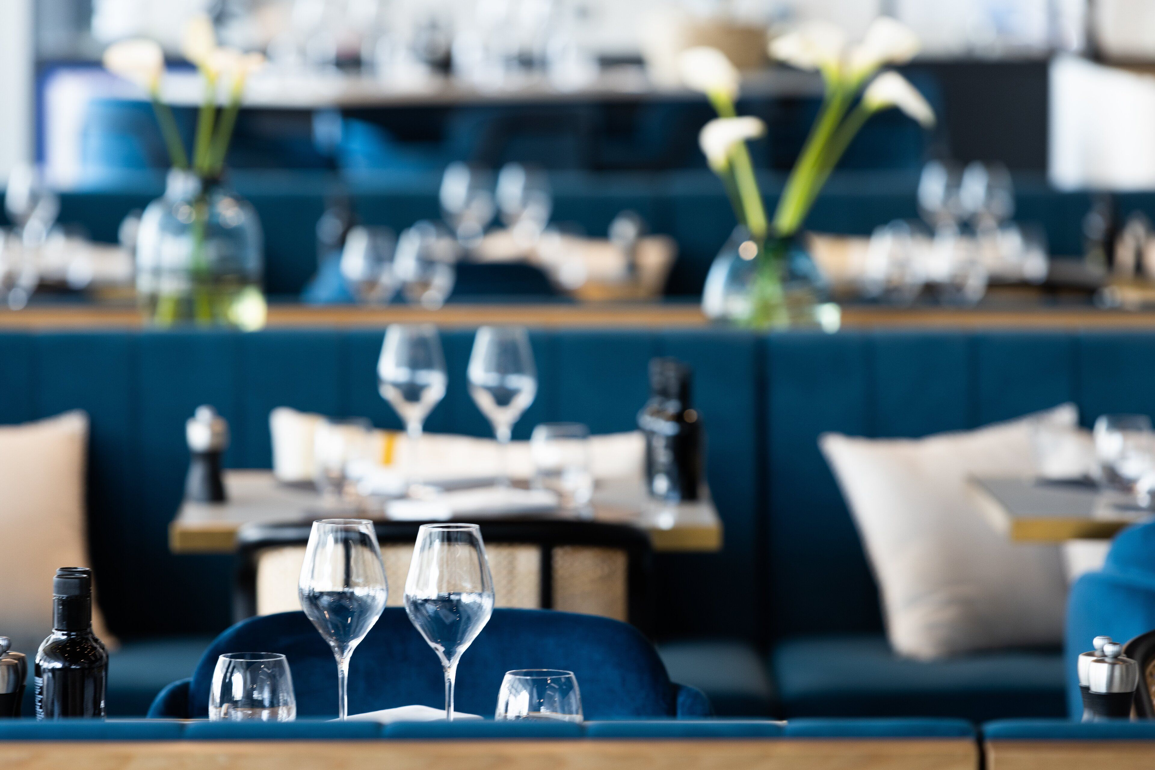 A restaurant interior with a blue couch, dining tables, and wine glasses.