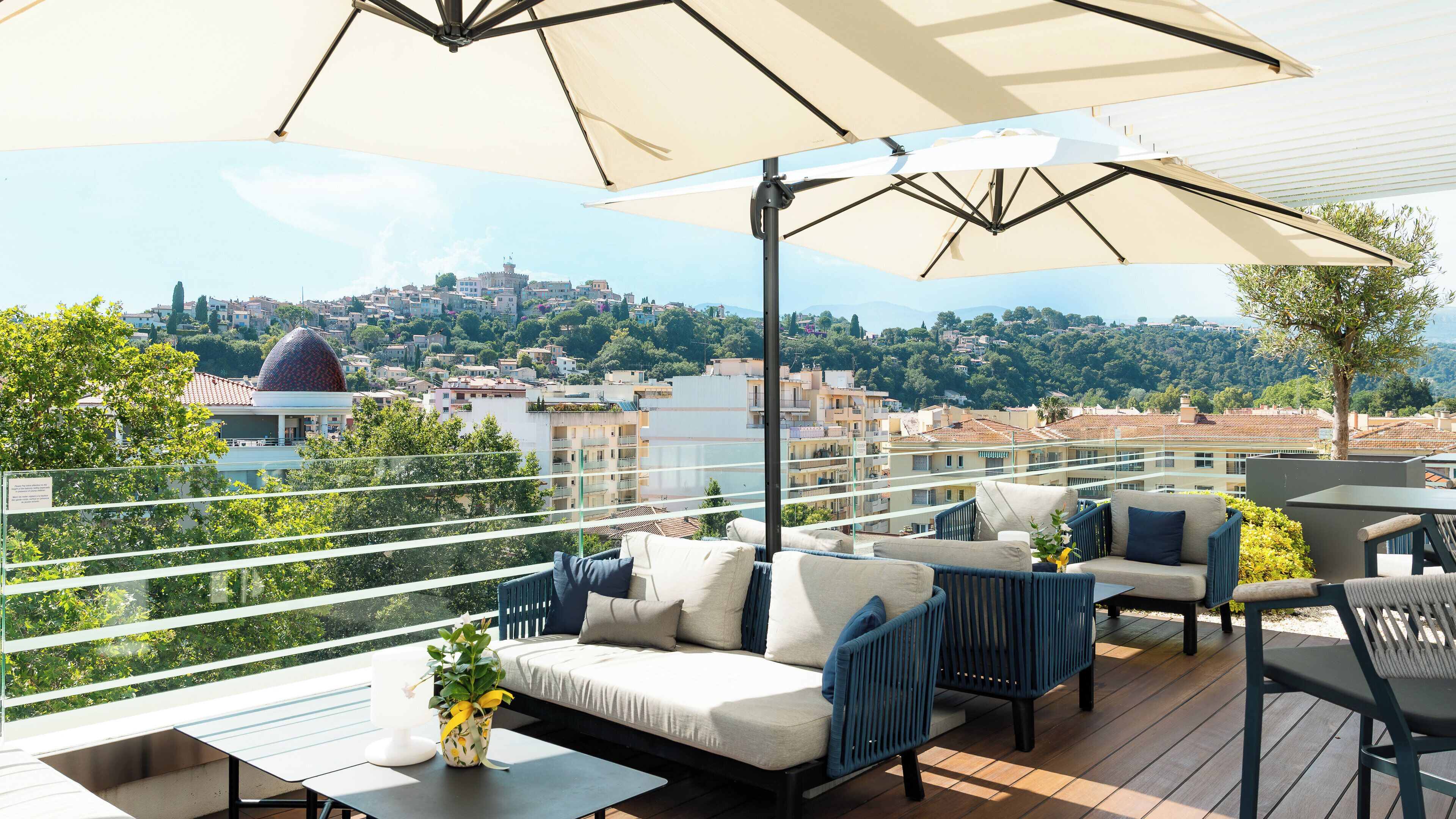 A rooftop terrace with outdoor furniture, a view of a cityscape, and a large umbrella providing shade.