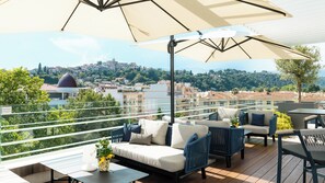 A rooftop terrace with outdoor furniture, a view of a cityscape, and a large umbrella providing shade. - Hotel Indigo Cagnes-sur-Mer by IHG (Cagnes-sur-Mer)