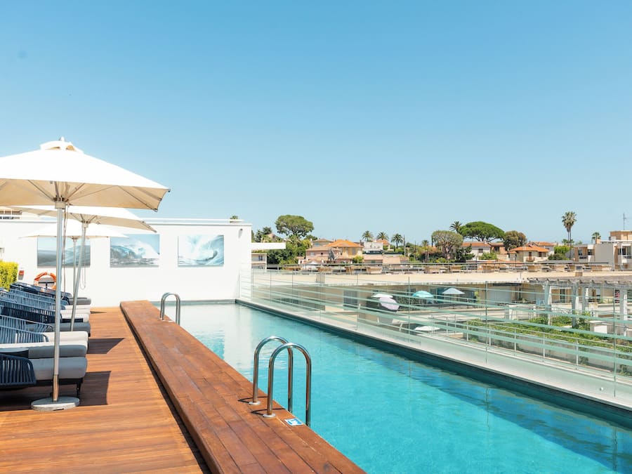 A poolside area with a wooden deck, lounge chairs, and umbrellas.