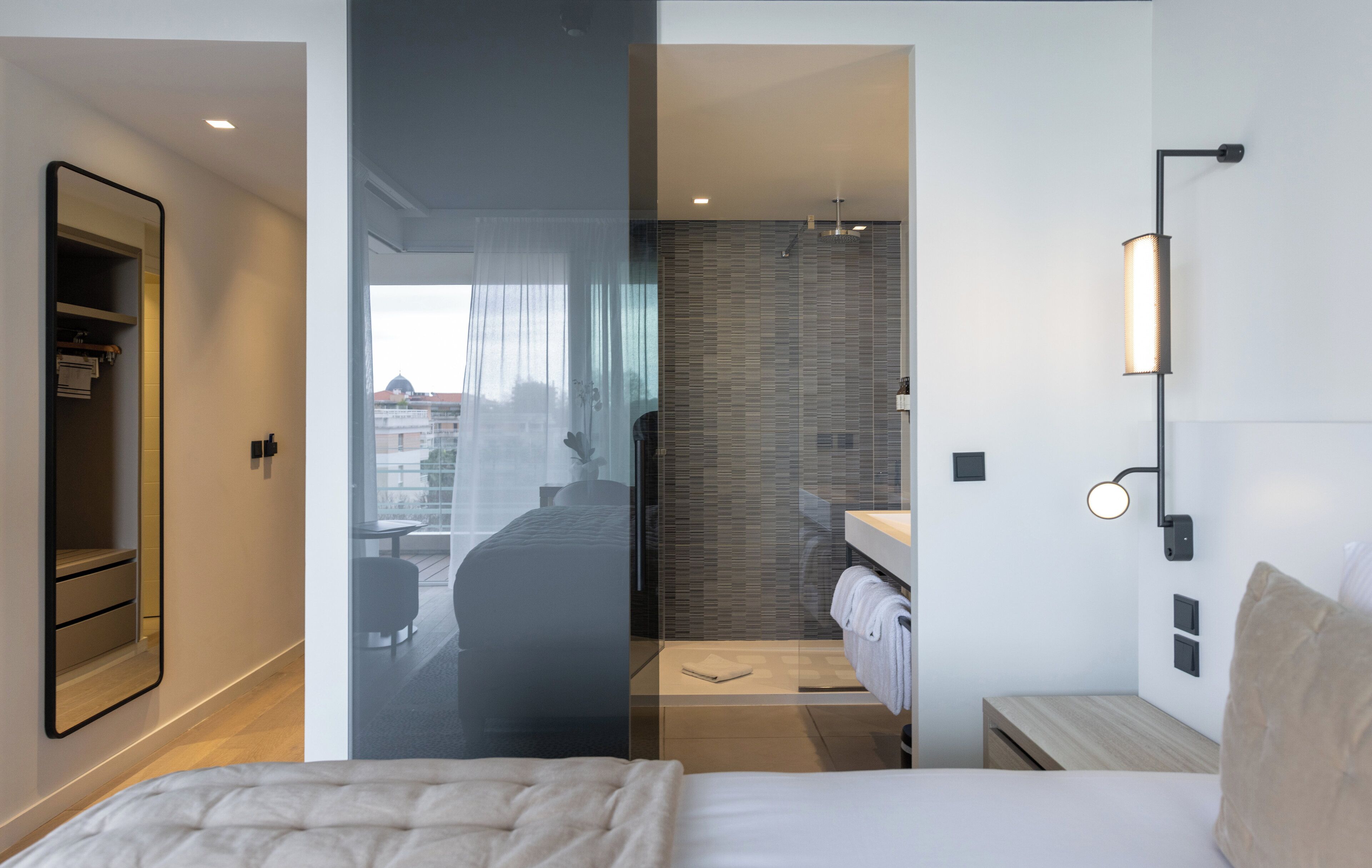 A modern hotel room with a large bed, a bathroom with a glass partition, and a view of the city.