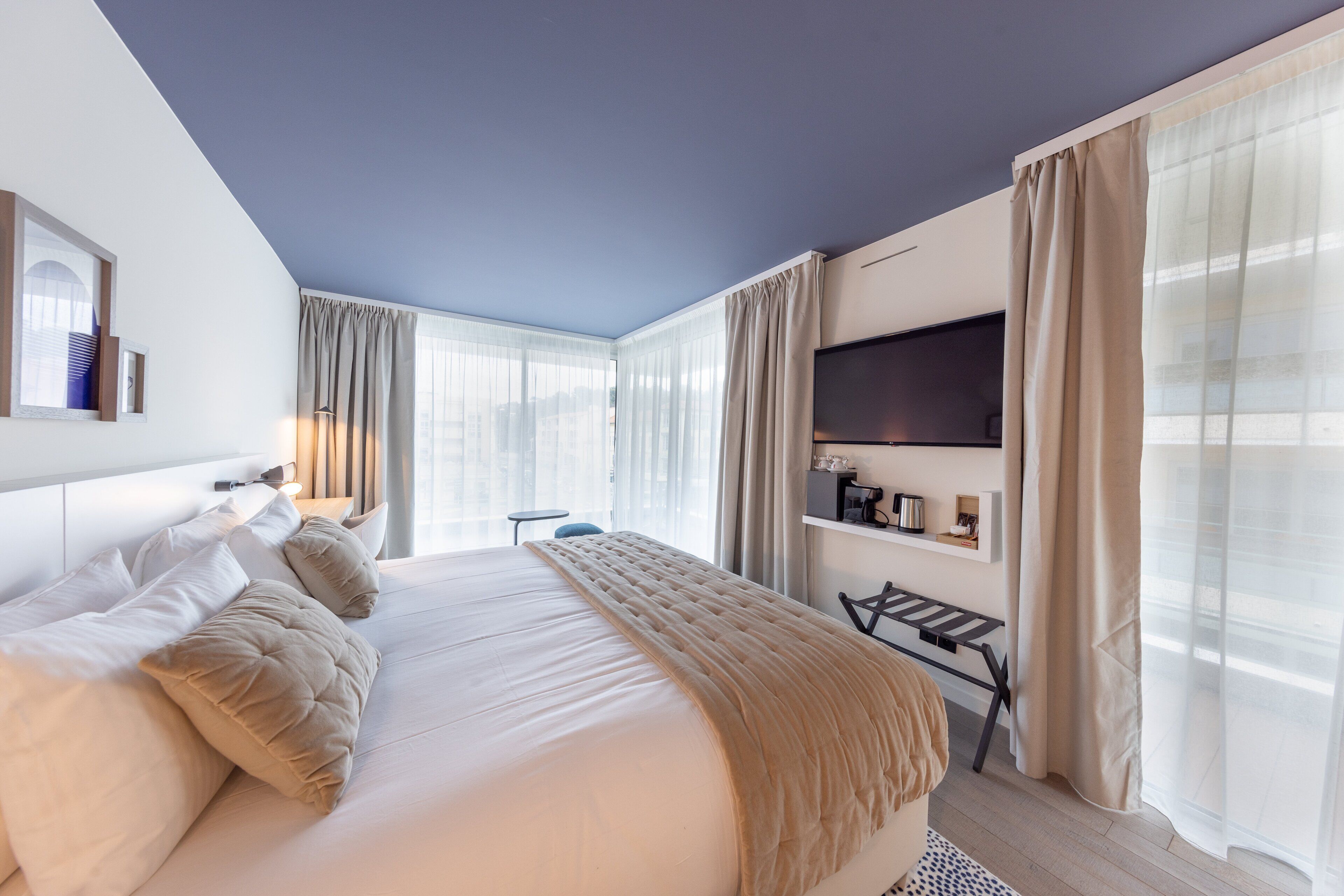 Habitación de hotel moderna con una cama grande, televisión de pantalla plana, escritorio y vistas de la ciudad a través de amplios ventanales.