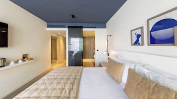 Habitación de hotel con una cama grande, televisor de pantalla plana, mesita de noche y baño visible a través de una puerta abierta.