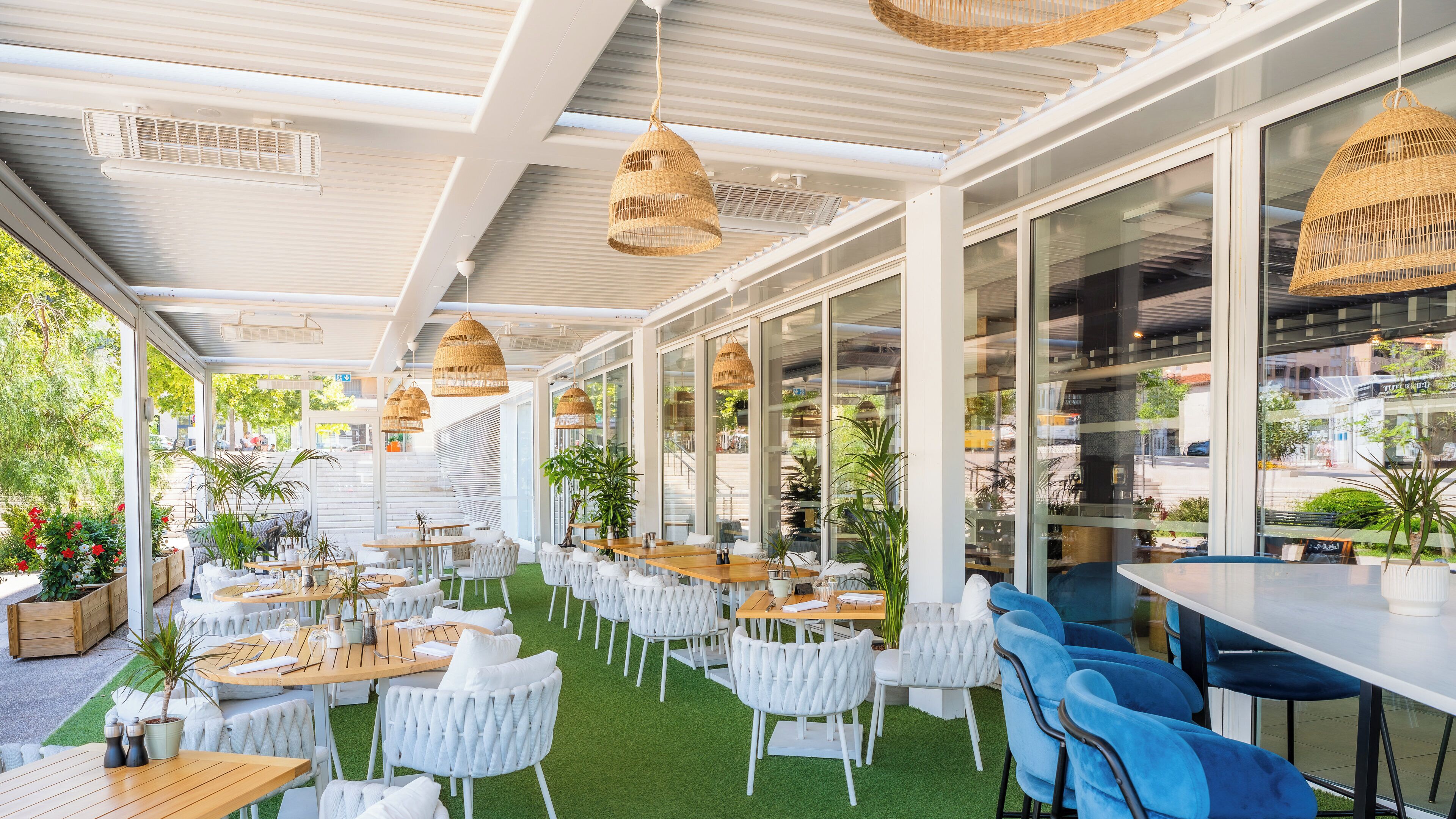 An outdoor seating area with tables and chairs, large windows, and hanging wicker lamps.