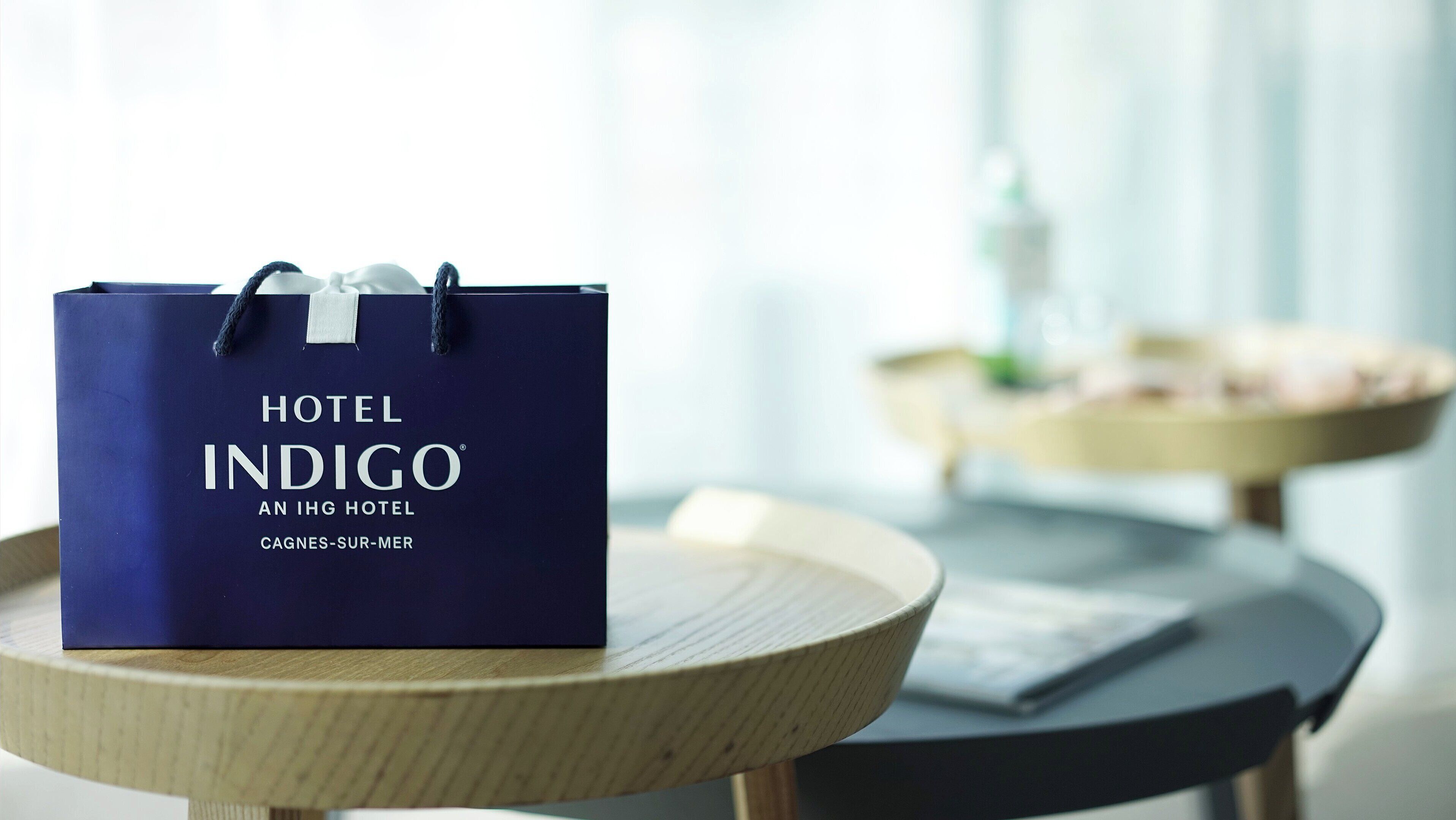 Un sac de voyage bleu, portant l’inscription « HOTEL INDIGO », est posé sur une table ronde en bois.