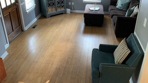 Ein geräumiges Wohnzimmer mit Holzboden, einem an der Wand befestigten Flachbildfernseher, einem dunkelgrauen Sofa und einem kleinen Beistelltisch.