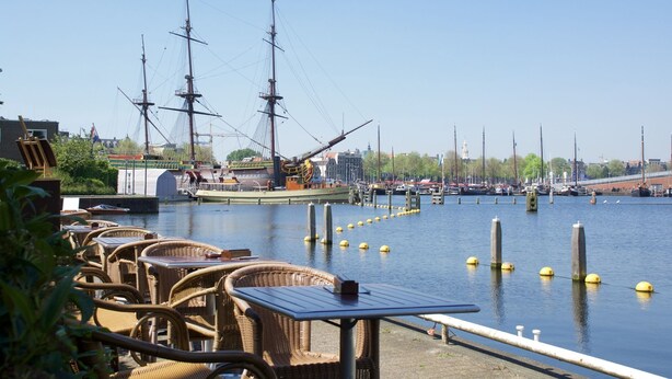 A waterfront restaurant with outdoor seating overlooking a marina with sailing ships. - Pension Homeland (Amsterdam)