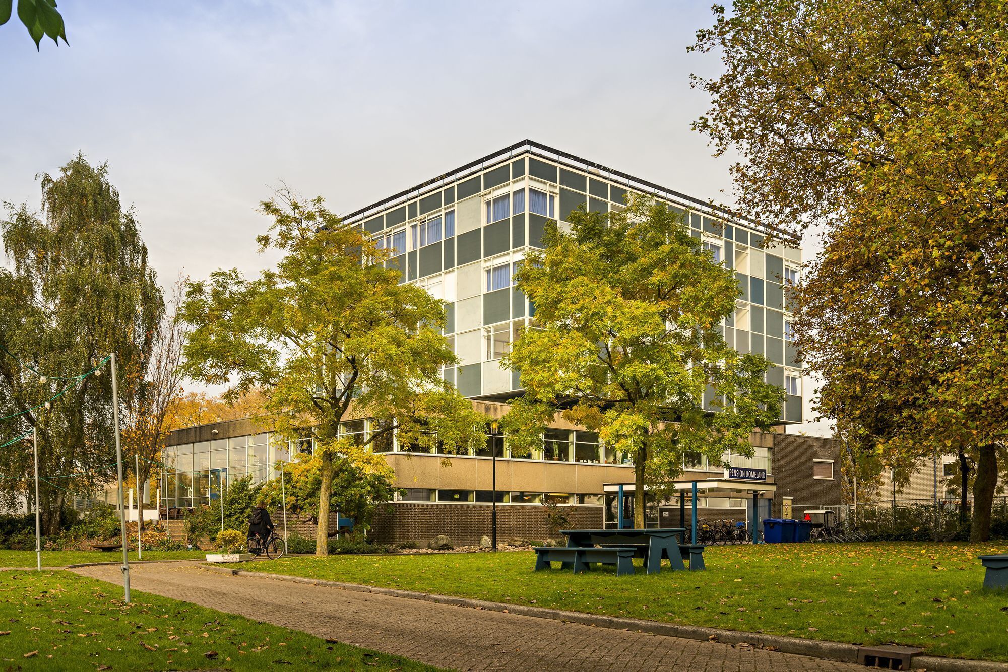A modern building with a glass facade, surrounded by trees and a paved walkway.