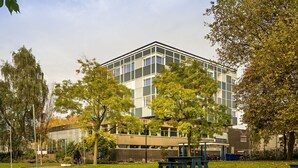A modern building with a glass facade, surrounded by trees and a paved walkway. - Pension Homeland (Amsterdam)