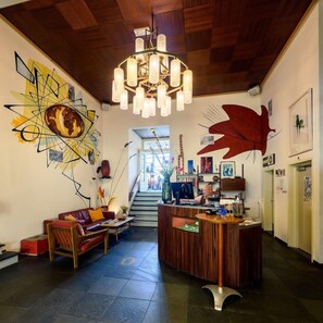 A lobby with a wooden ceiling, a reception desk, a staircase, and abstract wall art. - Pension Homeland (Amsterdam)