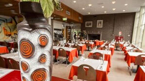 A dining area with tables set for service, a decorative vase with a leaf, and a brick wall in the background. - Pension Homeland (Amsterdam)