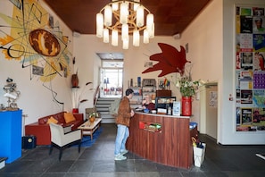 Um hall de entrada com balcão de recepção, um sofá vermelho, uma poltrona azul e uma grande pintura abstrata.