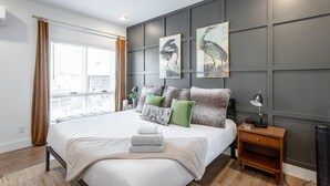 A modern bedroom with a large bed, a nightstand, and two wall-mounted lamps. - The Rhododendron - a PMI Scenic City Rental (Chattanooga)