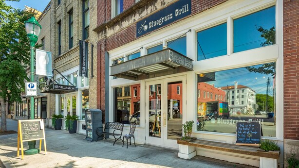 A storefront with a sign for Bluegrass Grill, a parking sign, and a chalkboard with messages. - The Rhododendron - a PMI Scenic City Rental (Chattanooga)