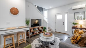 A modern living room with a TV, wooden furniture, a staircase, and a sofa with tiger print cushions. - The Rhododendron - a PMI Scenic City Rental (Chattanooga)