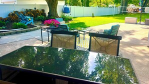 A backyard with a patio table, chairs, a basketball hoop, and a well-maintained lawn.