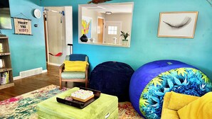 A room with a wooden chair, a green ottoman, a blue bean bag, a colorful rug, and a mirror with a map.