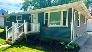 A single-story house with a front porch, a small deck, and a front yard with plants.