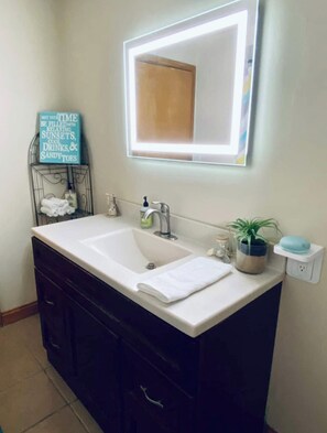 Casa de banho com uma sanita branca, armários escuros, um espelho com iluminação LED, um porta-toalhas e uma pequena planta em vaso.
