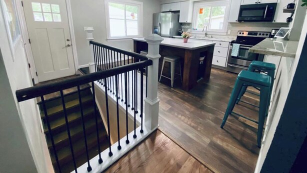 A modern kitchen with white cabinets, stainless steel appliances, and a wooden floor.