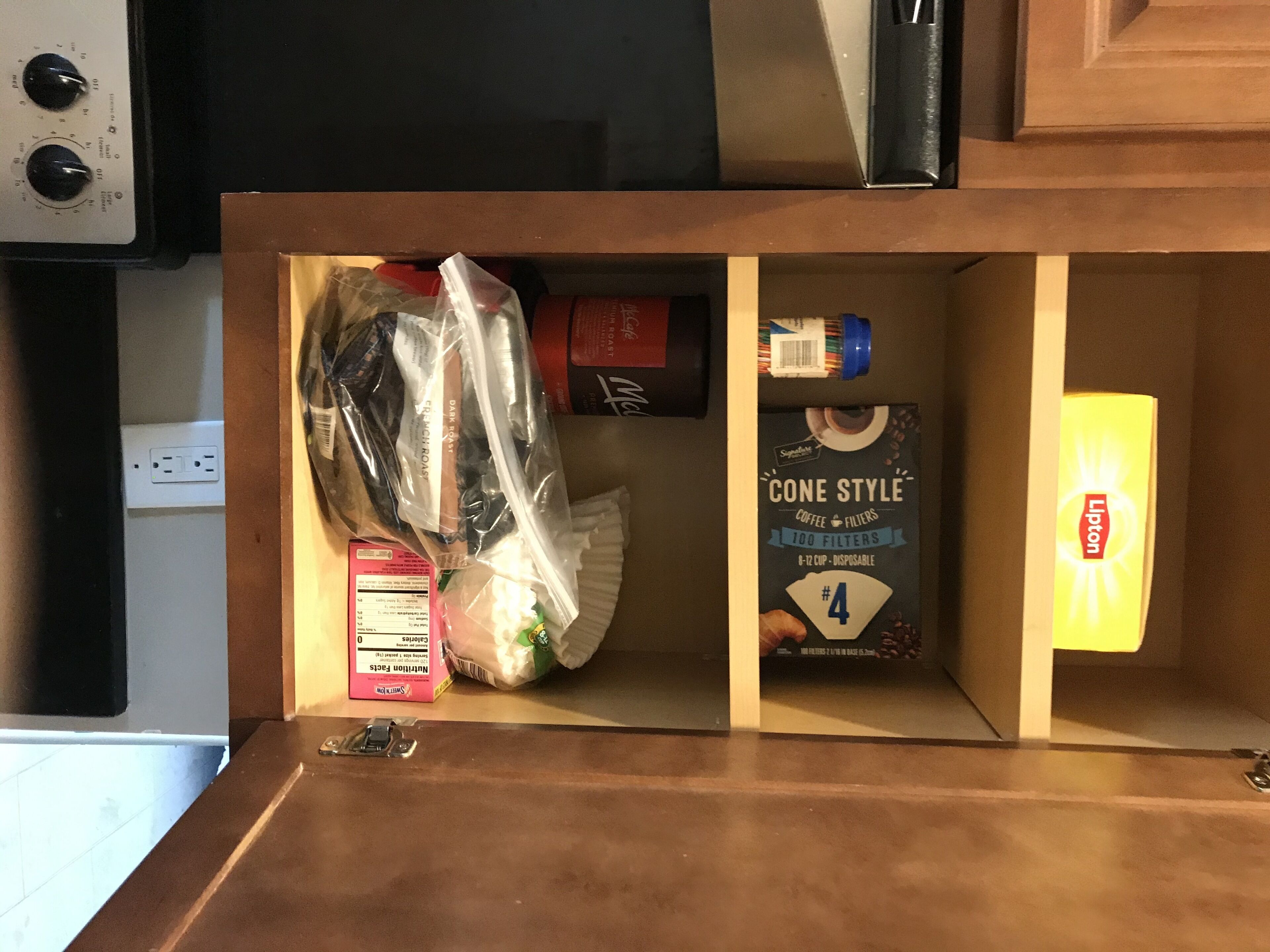 A kitchen cabinet with a microwave above, a coffee maker, and a box of coffee filters.